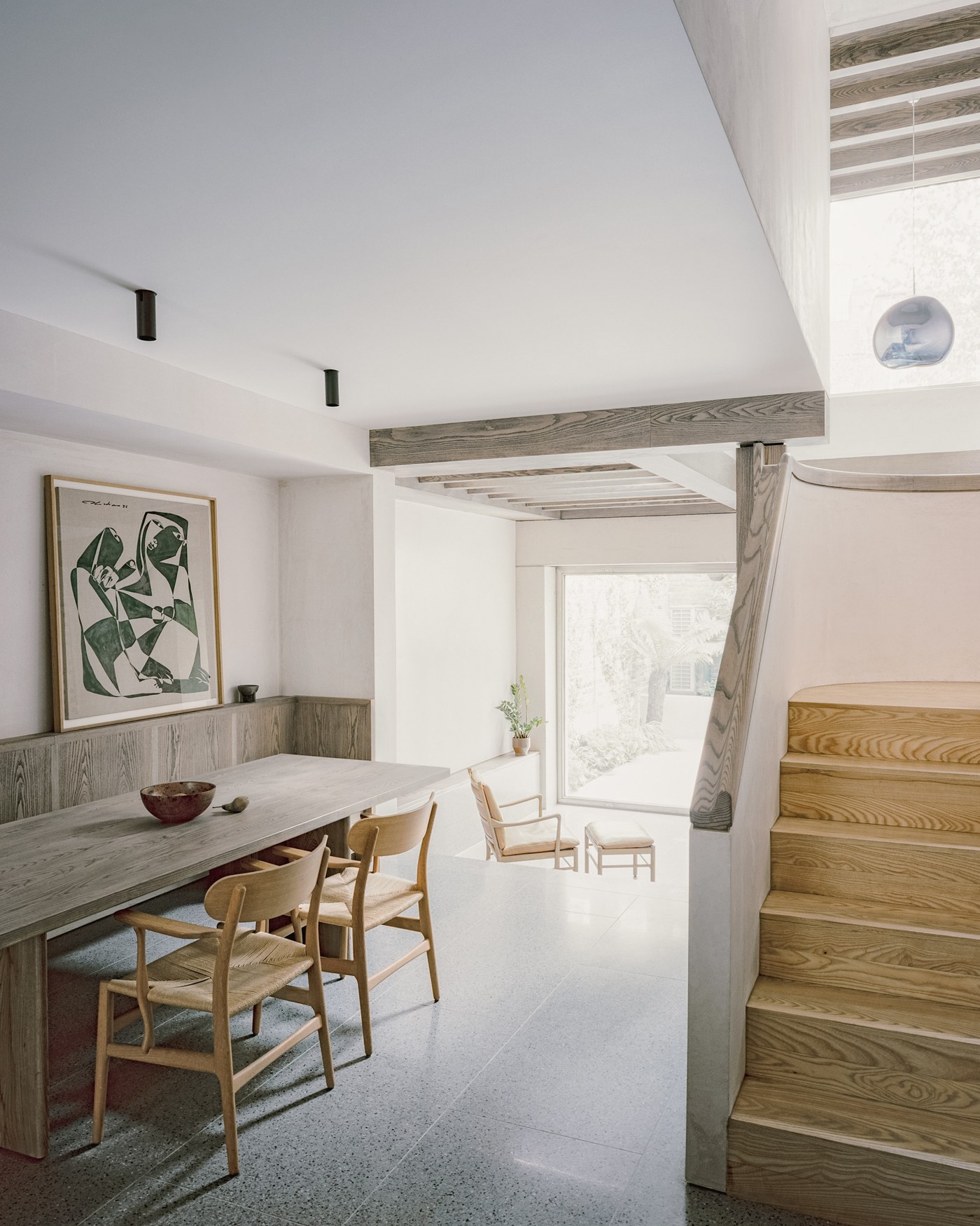 Caithness Road W14 — dining area with a long timber table beside the ash staircase, and the garden at the far end of the house