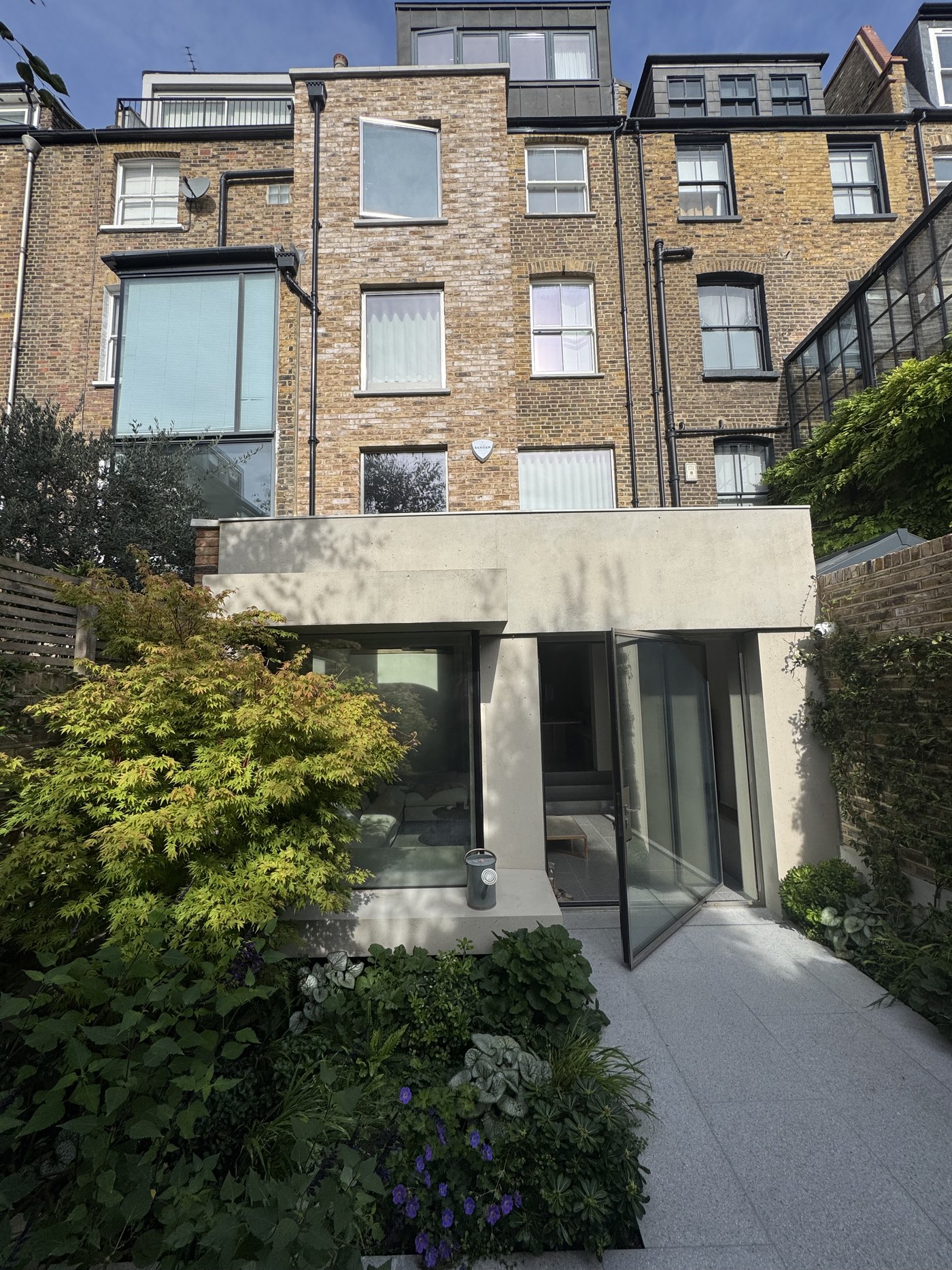 Caithness Road W14 — the rear of the house from the garden: the three-storey outrigger above the concrete ground-floor extension, with its fixed window and pivot door