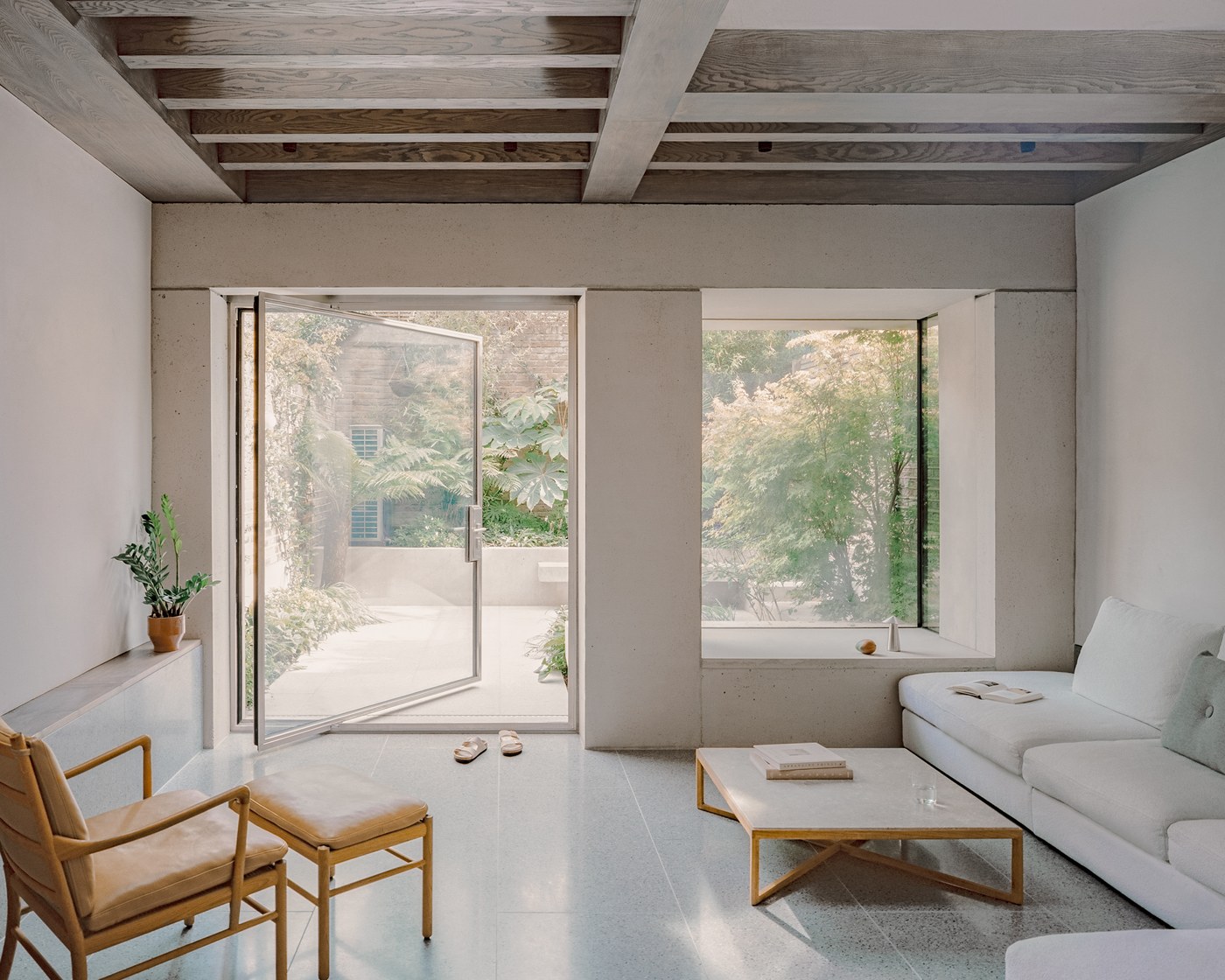 Caithness Road W14 — rear reception room under exposed timber beams, with a full-height pivot door and a deep-set window looking onto the garden