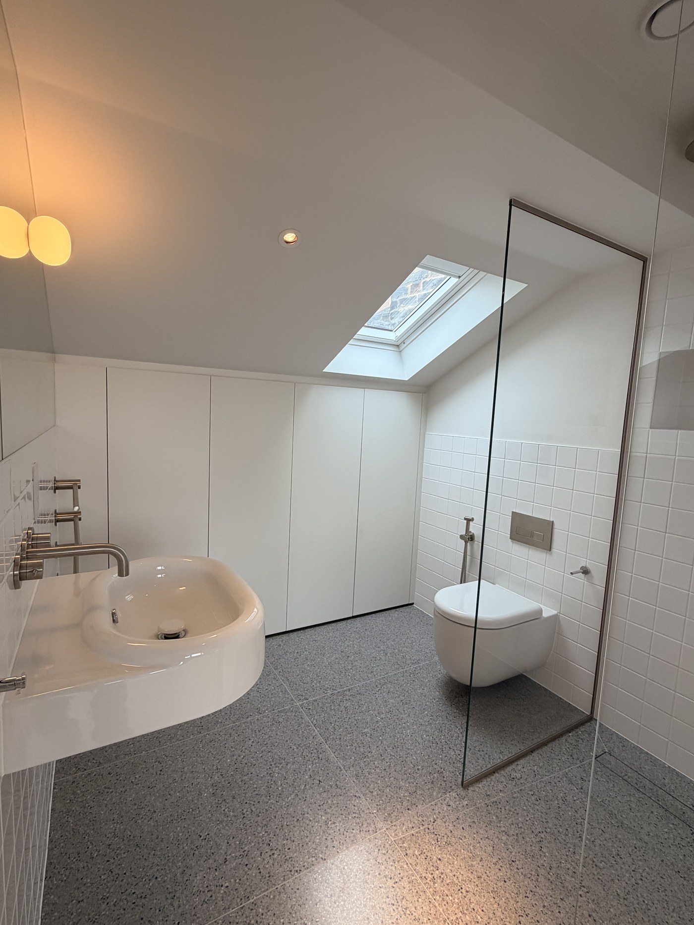 Caithness Road W14 — top-floor shower room under a rooflight, with a frameless glass screen, wall-hung basin and WC, and speckled stone floor