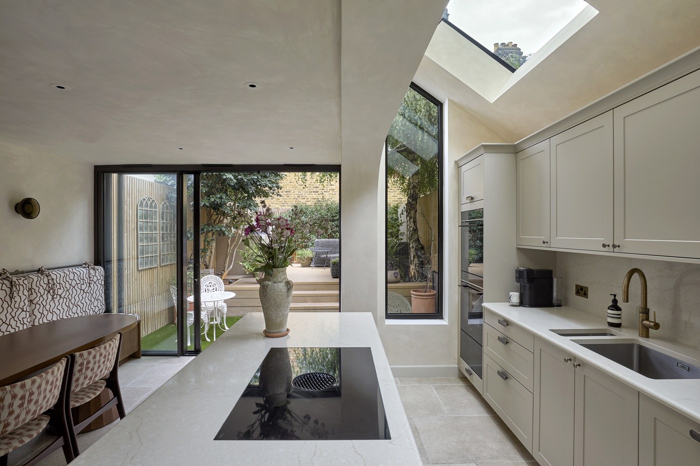 Honeywell Road SW11 — kitchen extension with a stone-topped island, a rooflight overhead and slim black-framed aluminium doors opening onto the garden